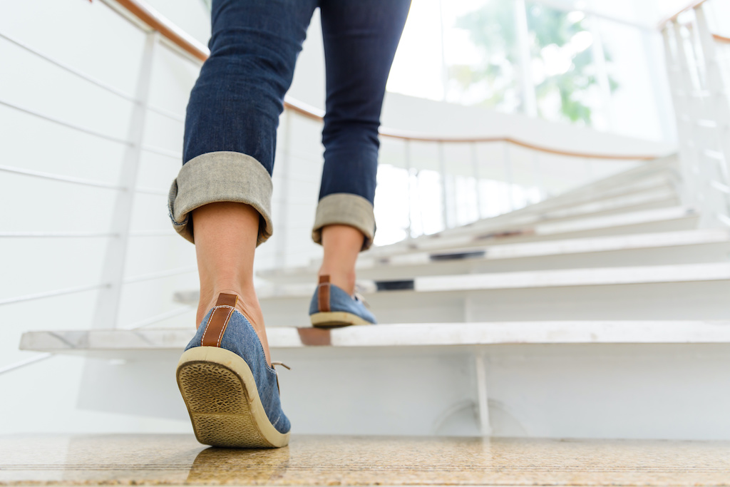 Young adult woman walking up the stairs with sun sport background.