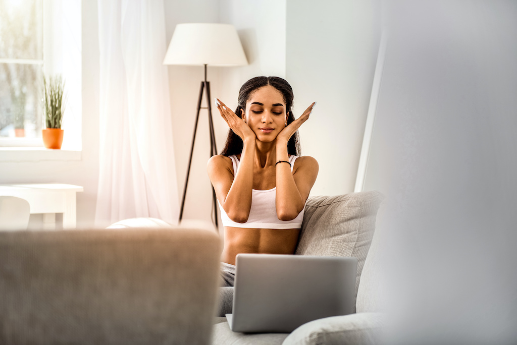 So pleased. Beautiful international woman looking downwards at laptop while doing face massage