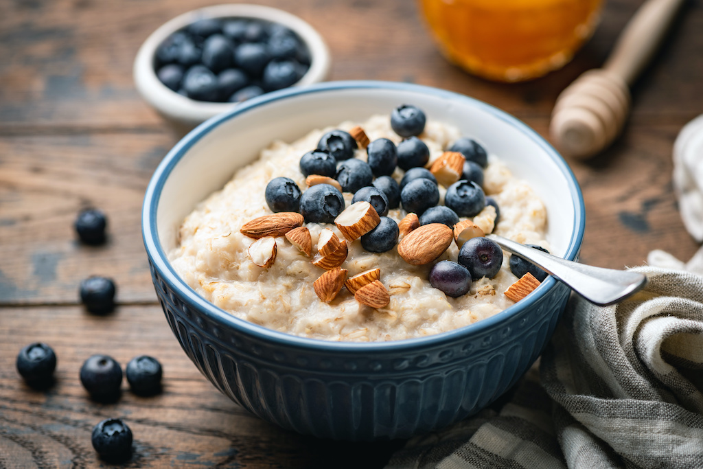 Oatmeal porridge with blueberries, almonds in bowl on wooden table background. Healthy vegetarian 
breakfast food