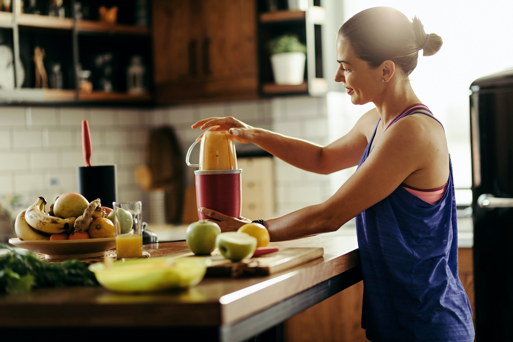 Smiling-athletic-woman-blending-fresh-fruit-and-preparing-healthy-smoothie-in-the-kitchen