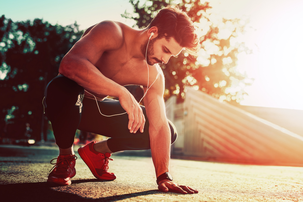 Young male jogger athlete training and doing workout outdoors in city.