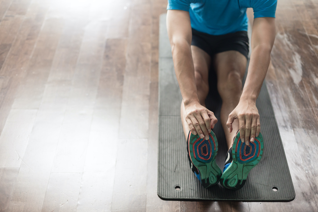 High-angle view of the hands of a man touching his toes from sitting position, as a stretching exercise for flexibility at home or at the gym