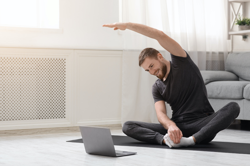 Quarantine sport. Young man practicing fitness with online training on laptop, free space