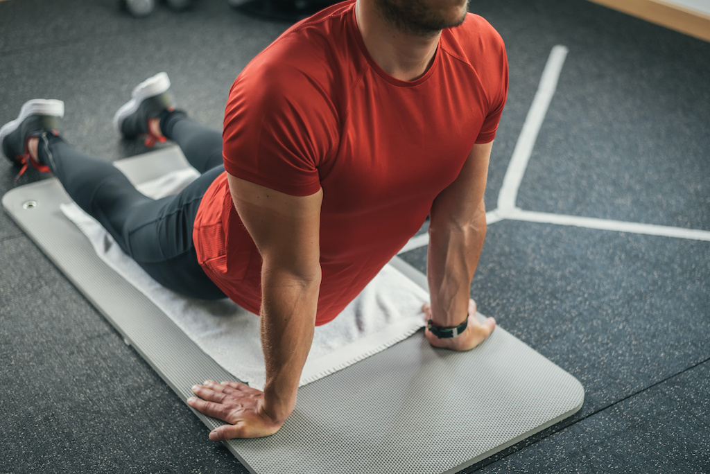 Sporty man stretching back before gym workout. Fitness strong male athlete on floor mat and towel warming up indoor.