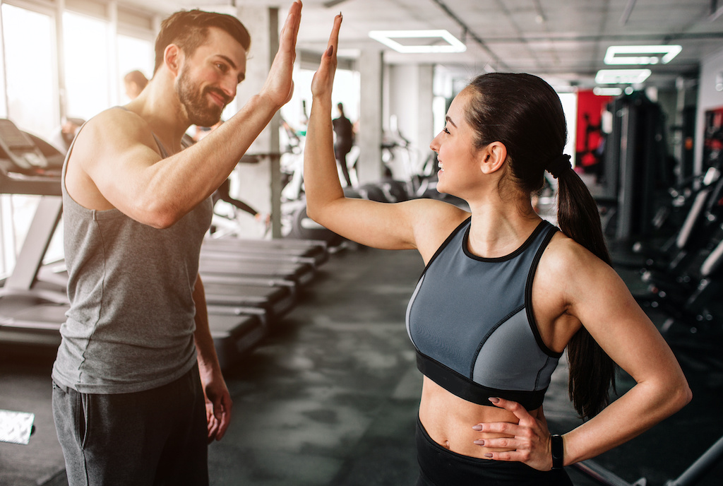 A beautiful girl and her well-built boyfriend are greeting each other with a high-five. They are happy to see each othr in the gym. Young people are ready to start their workout
