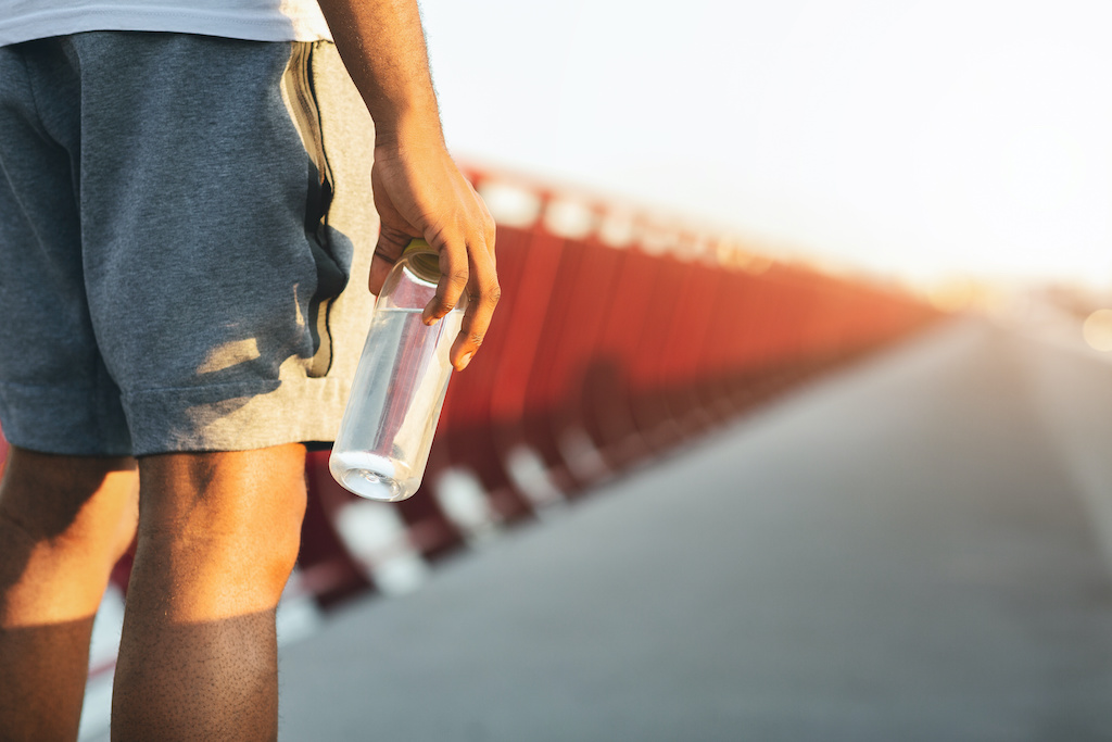 Hydrating concept. Afro Man Holding Bottle Of Water, staying on the bridge in sun lights, empty space